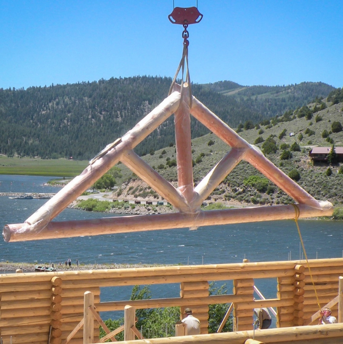 log truss being set by a crane at cabin on a lake